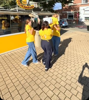 Het gele paviljoen van Frituur Marina met het ronde Frituur Marina-bord, onder een grote boom, met medewerkers in gele T-shirts op het terras