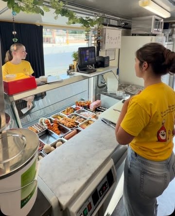 Achter de toog van Frituur Marina: medewerkers in gele T-shirts en een toonbank vol snacks